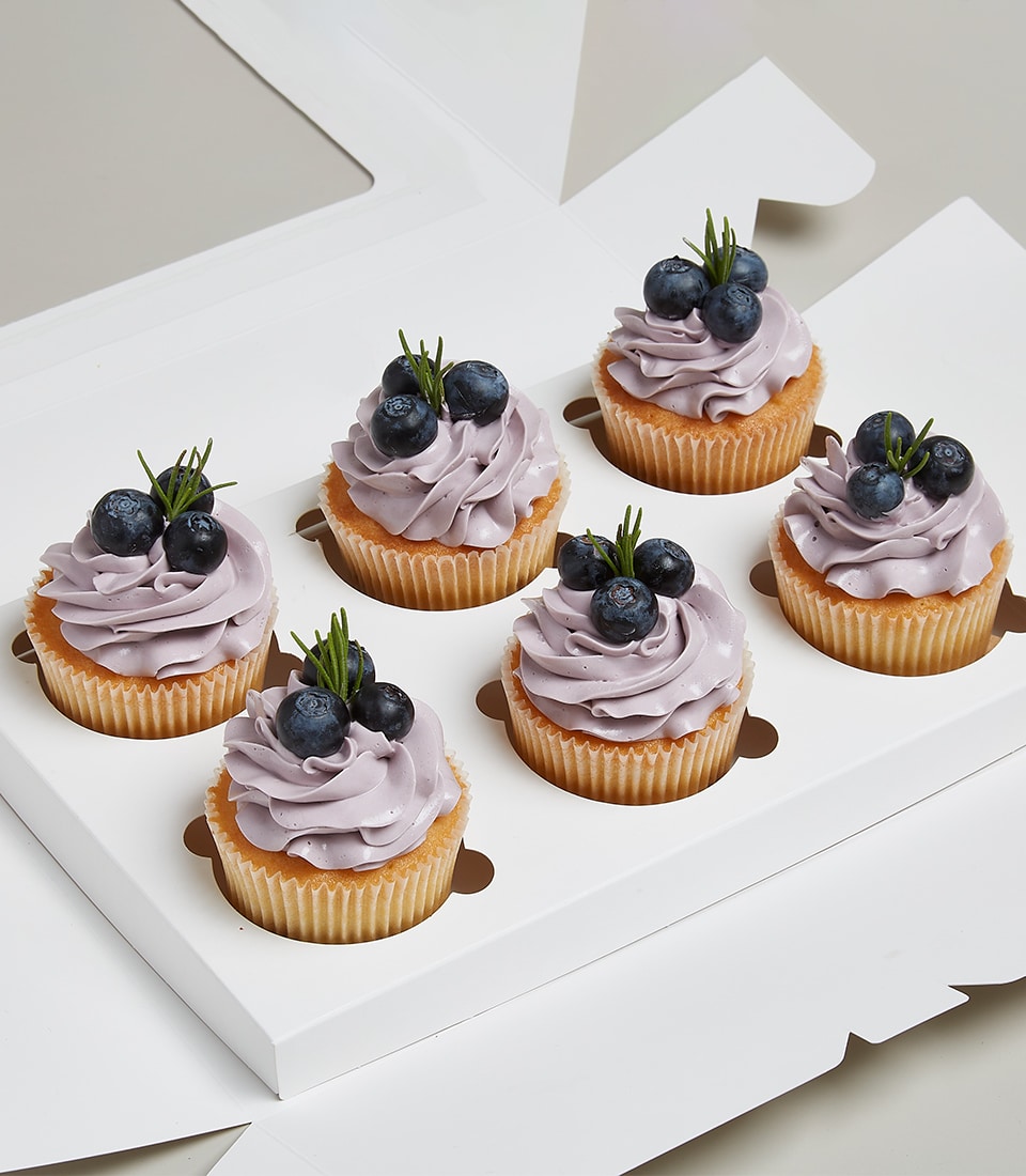 Six blueberry cupcakes with purple frosting and fresh berries in white gift box