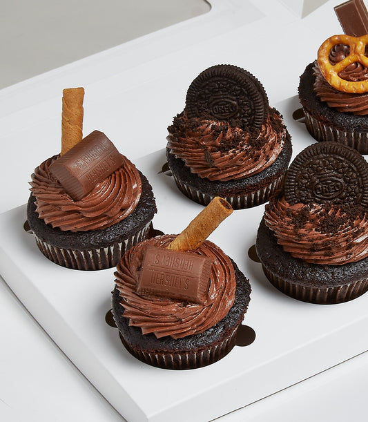 Assorted chocolate cupcakes with milk chocolate frosting, candy bars, and cookies in a white gift box