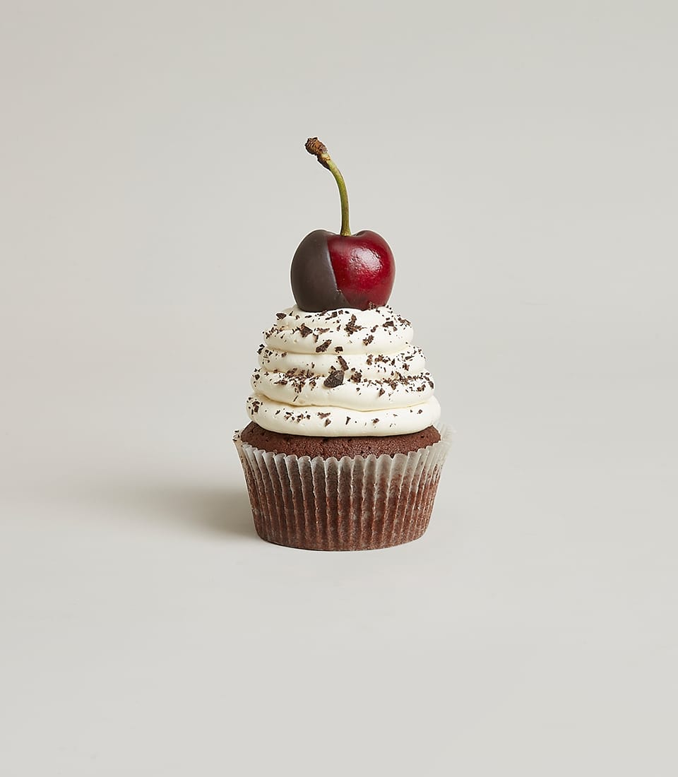 Dark chocolate cupcake with white frosting, chocolate cookie crumbs, and chocolate-dipped cherry