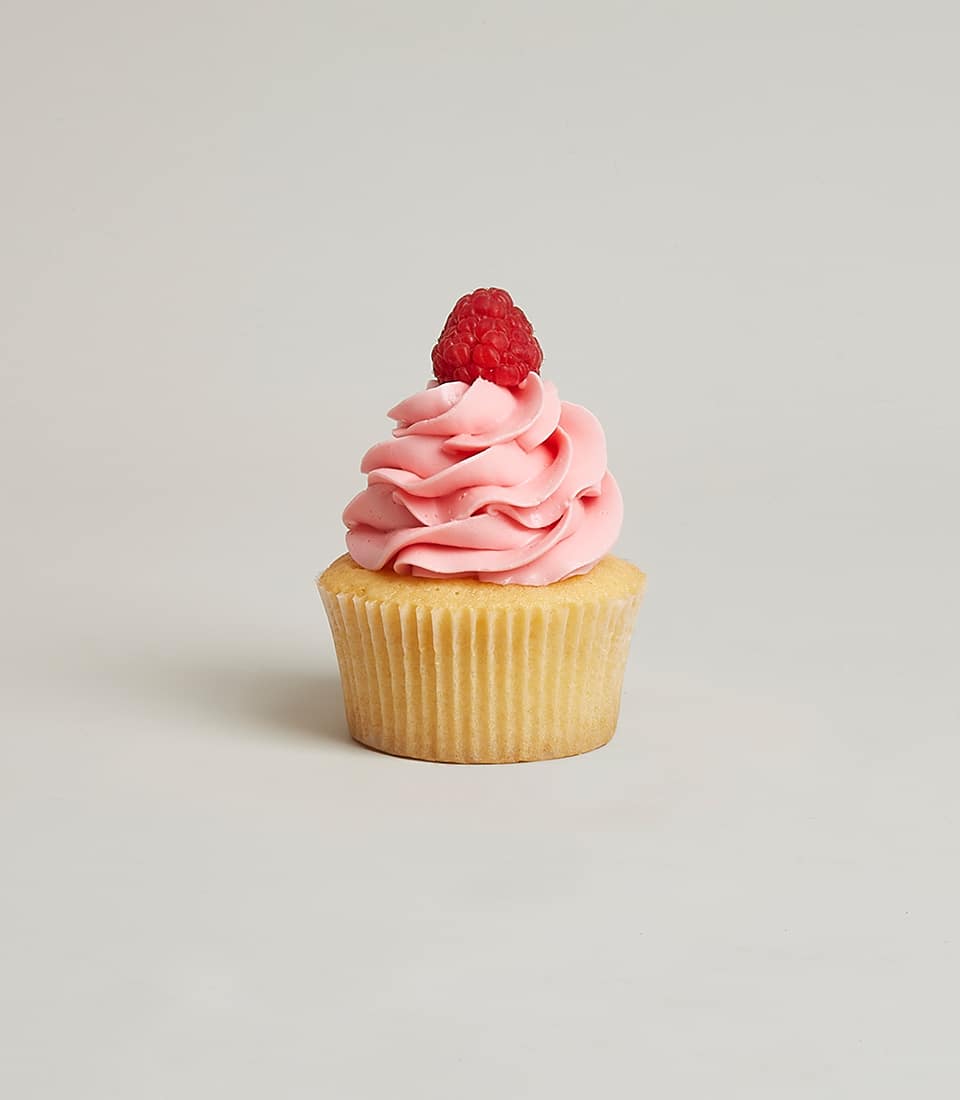 Raspberry jam-centred vanilla cupcake with pink frosting and fresh berry garnish
