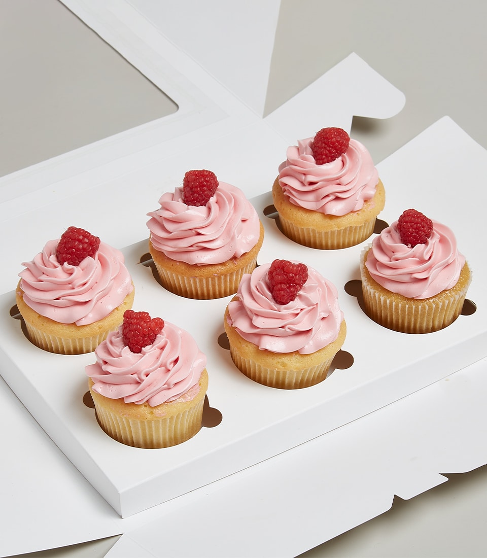Six vanilla cupcakes with raspberry jam centers, pink frosting swirls, and fresh red raspberries in white gift box