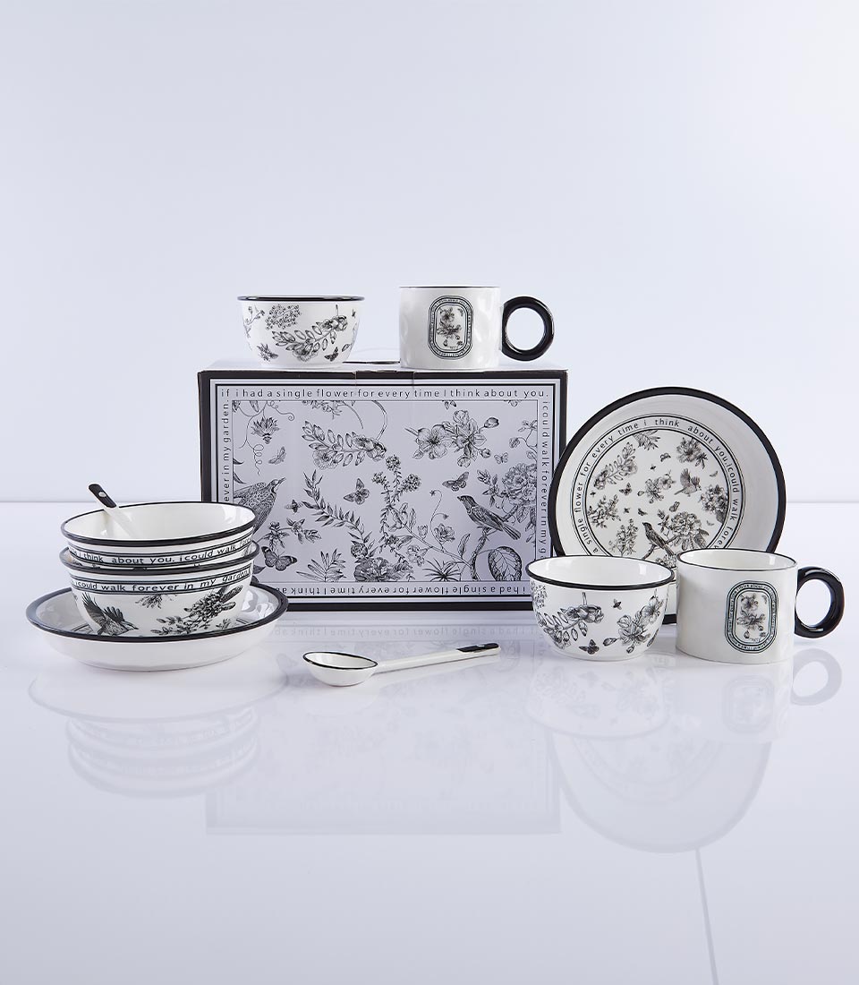 Vintage floral ceramic dinnerware set with black botanical and bird illustrations on white, includes bowls, mugs, and plate