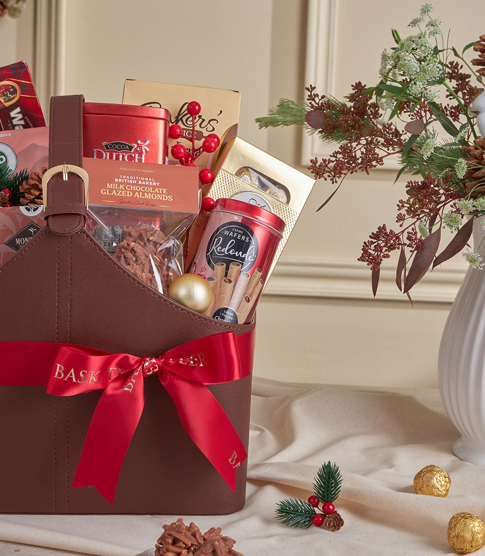 Brown leather tote filled with cocoa, coffee, and gourmet treats, red satin ribbon, luxury New Year gift basket