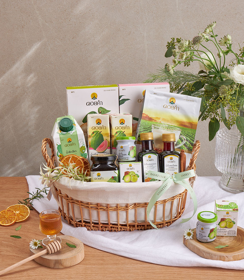 Woven wicker wellness gift basket with guava juice, honey, preserves, and natural botanicals tied with green ribbon