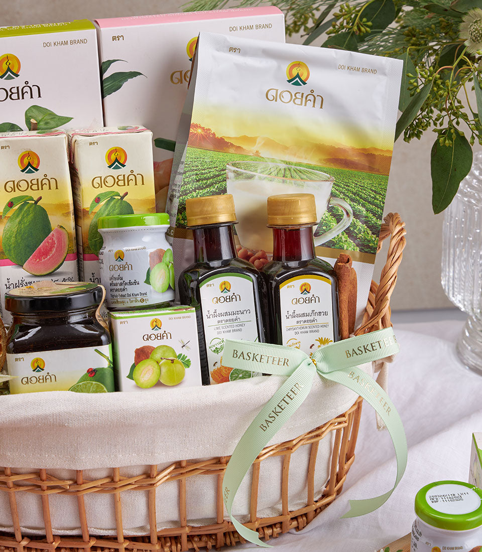 Premium woven wellness gift basket with Thai health products, golden-labeled boxes, and dark glass bottles tied with green