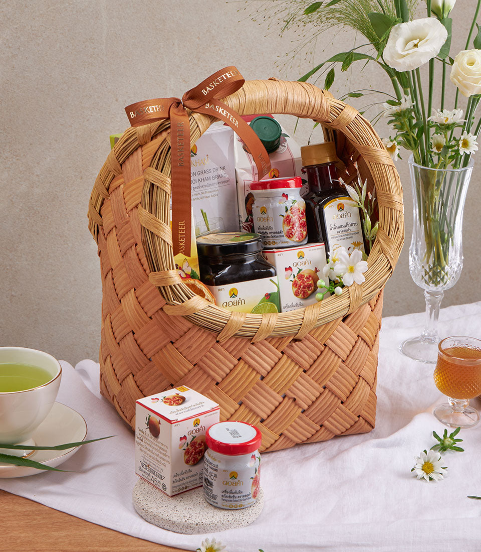 Woven wicker basket filled with herbal teas, wellness drinks, and gourmet jars with pomegranate designs, tied with brown