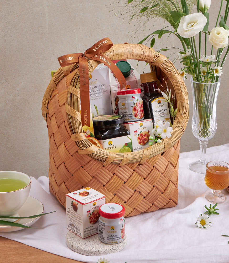 Woven wicker basket filled with herbal teas, pomegranate preserves, and wellness beverages in glass jars and bottles, tied