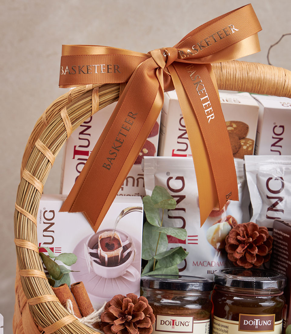 Woven straw gift basket with DoiTung coffee, macadamia, and artisan gourmet items tied with gold satin ribbon