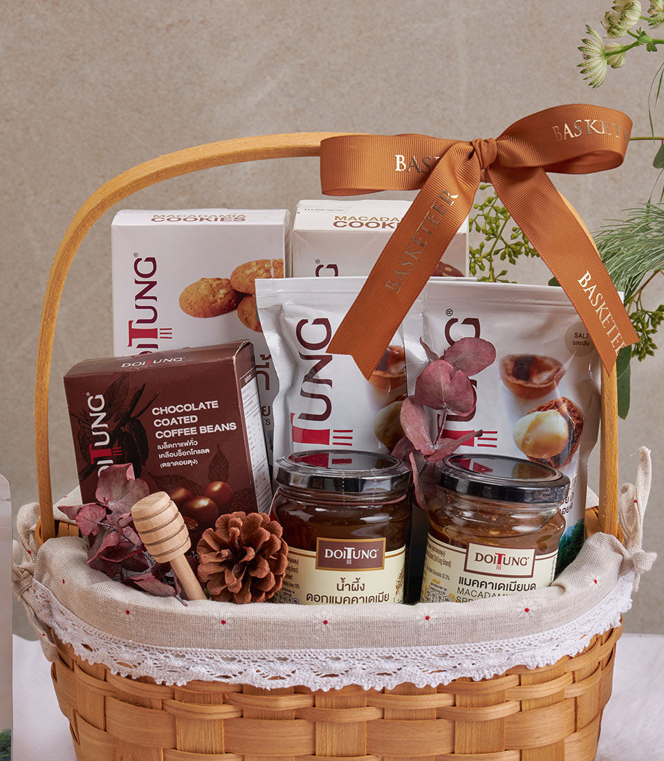 Woven gift basket with DoiTung macadamia nuts, honey jars, coffee beans, and gourmet treats tied with brown ribbon