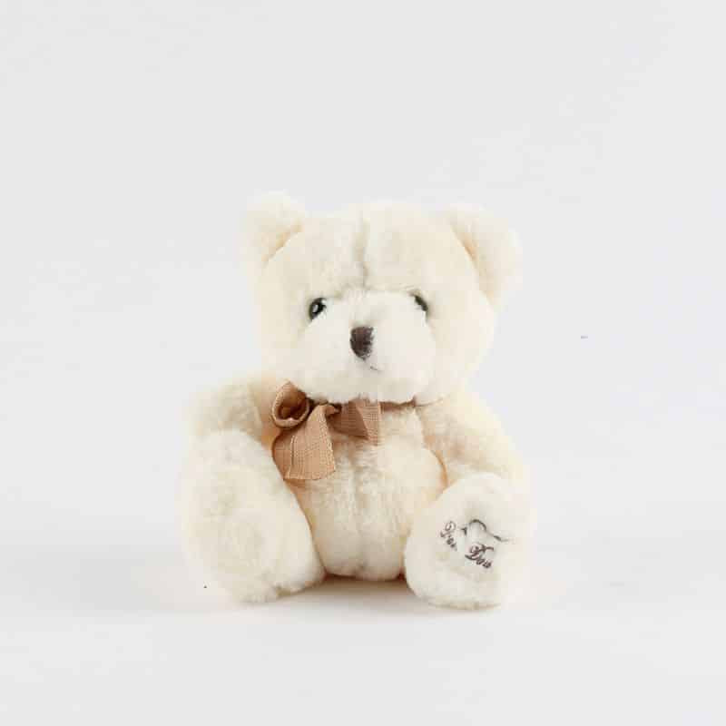Cream plush teddy bear with bow and embroidered heart detail, perfect for gifting