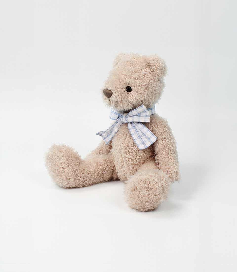 A tan, fluffy teddy bear with a blue plaid bow, ready to be included in a Basketeer premium hamper delivery in Thailand.