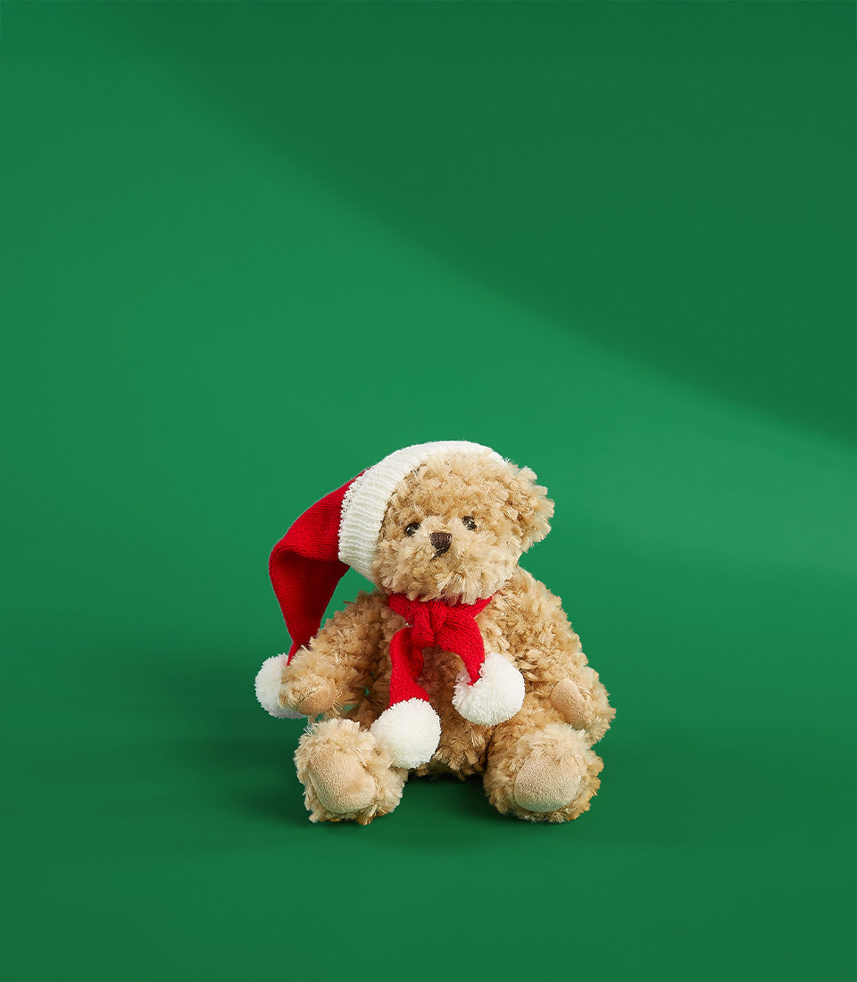 Soft plush teddy bear wearing red and white Santa hat and pom-pom scarf, festive gift add-on