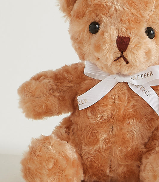 Light brown fluffy teddy bear with embroidered features and white satin bow ribbon, perfect for gifting