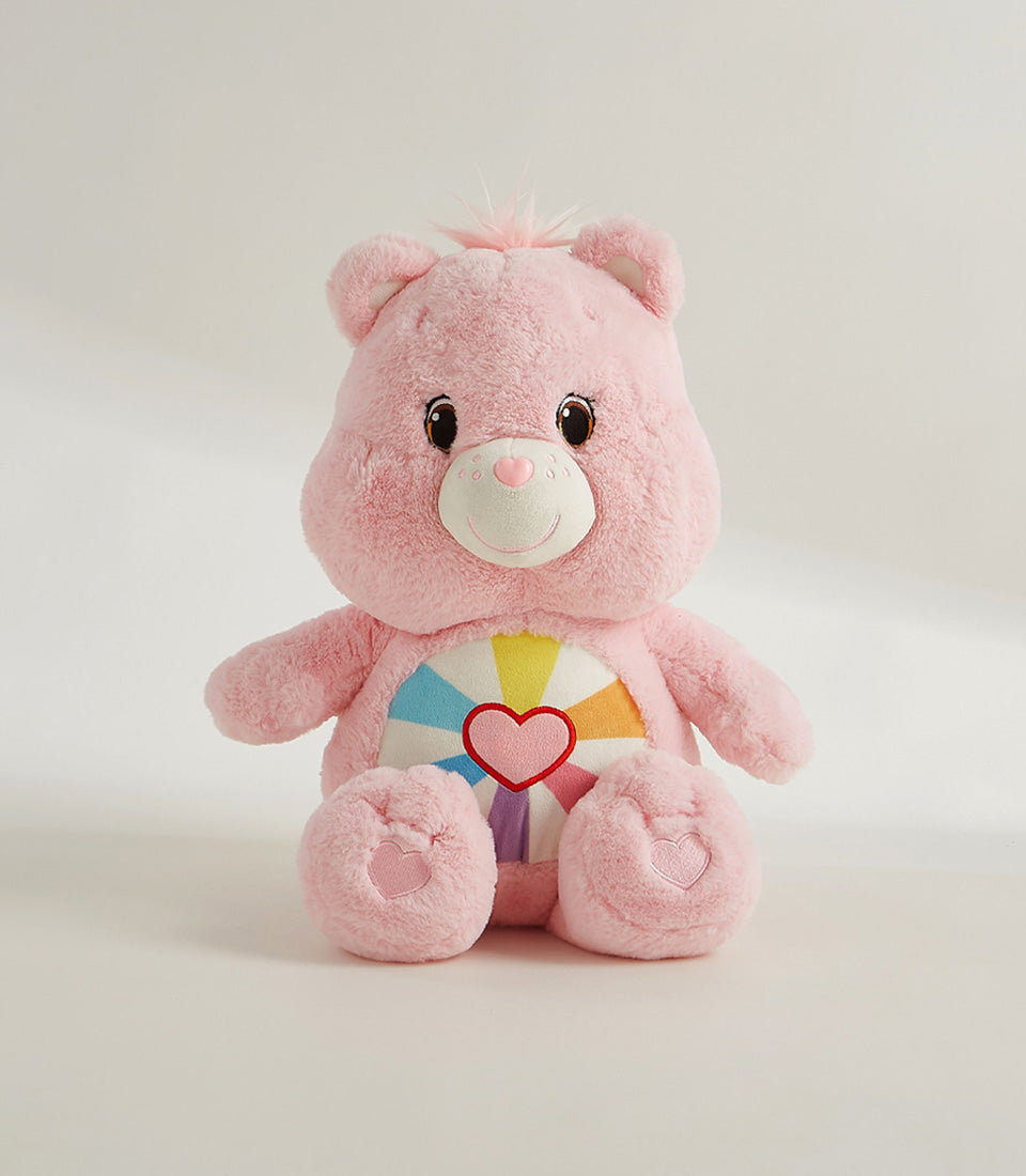 Soft pink plush Care Bear with rainbow heart belly emblem and embroidered paw details