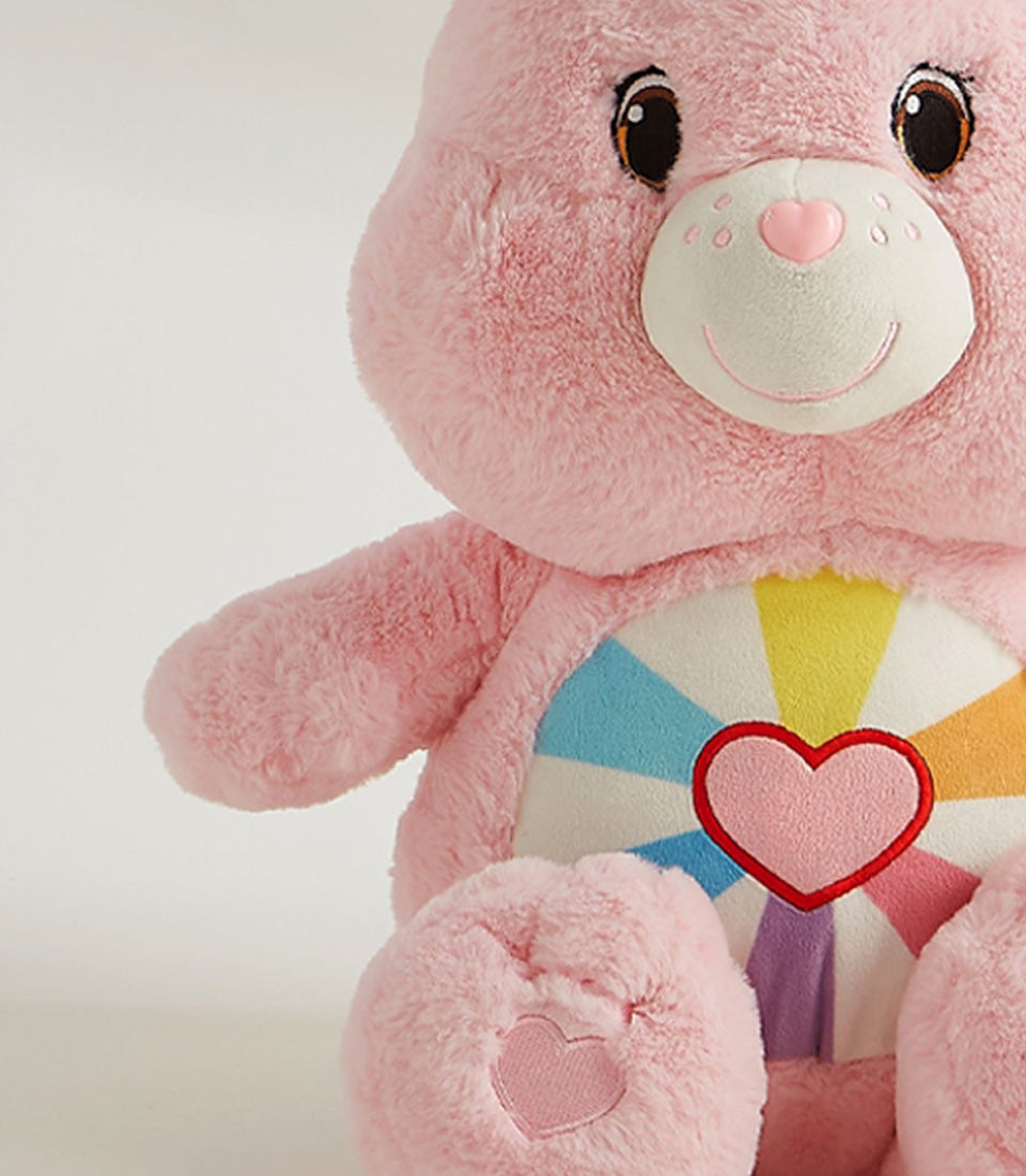 Pink plush teddy bear with heart motif and rainbow belly design, soft cuddly stuffed toy for gifting