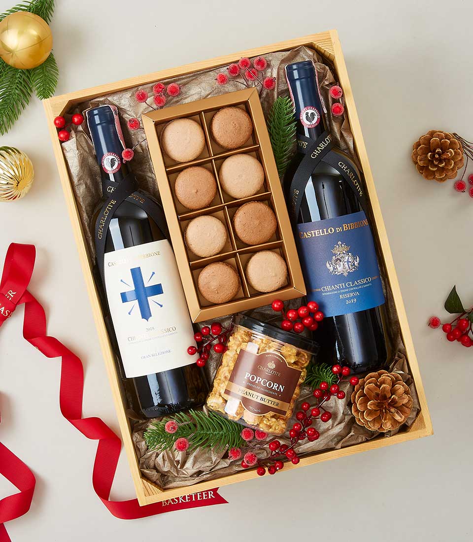 Festive wooden crate gift box with Chianti and Chardonnay wines, Charlotte macarons, gourmet popcorn, and holiday greenery