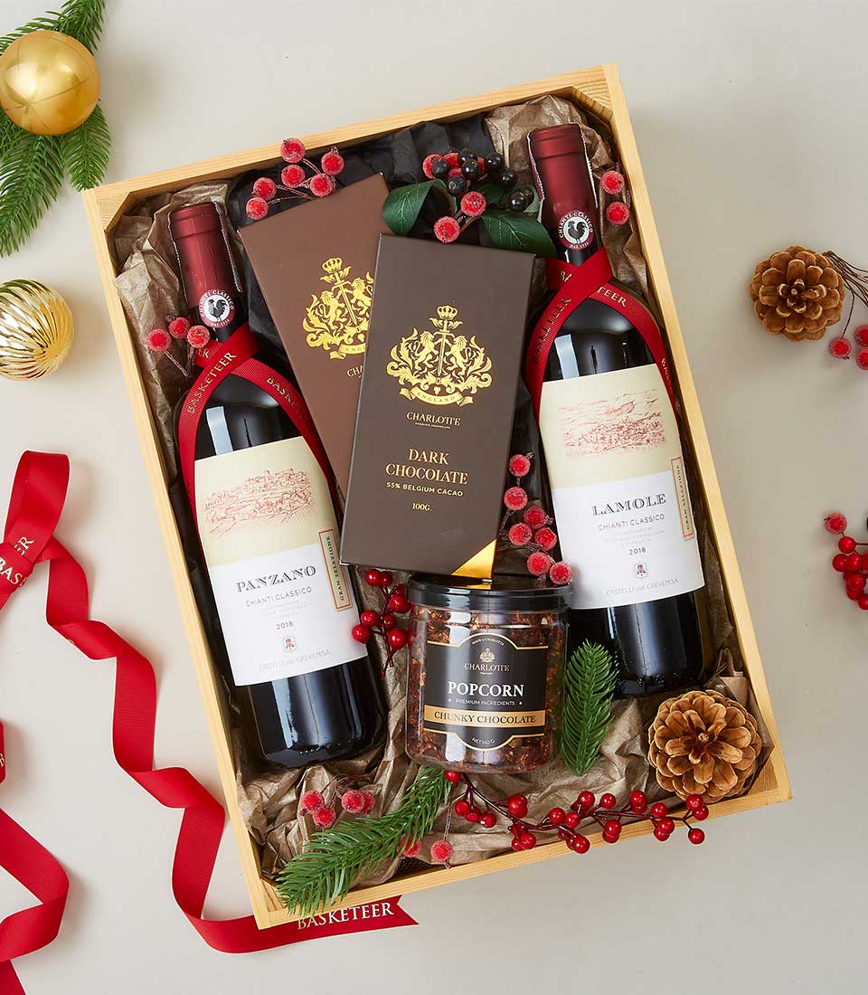 Luxury gift box with two red wines, Belgian dark chocolate bars, and gourmet popcorn, decorated with festive berries and pine