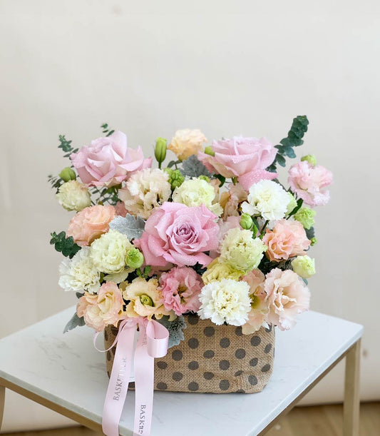 Blooming Bright pastel flower basket with pink roses, carnations, and peach blooms in rustic burlap container