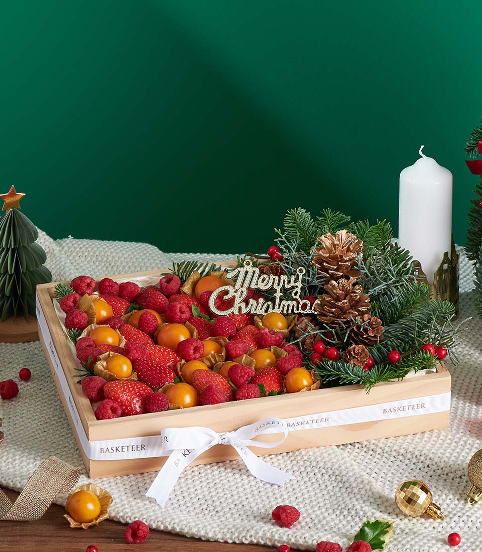 Festive wooden gift box filled with fresh strawberries, raspberries, and golden physalis with Christmas ornament and pine