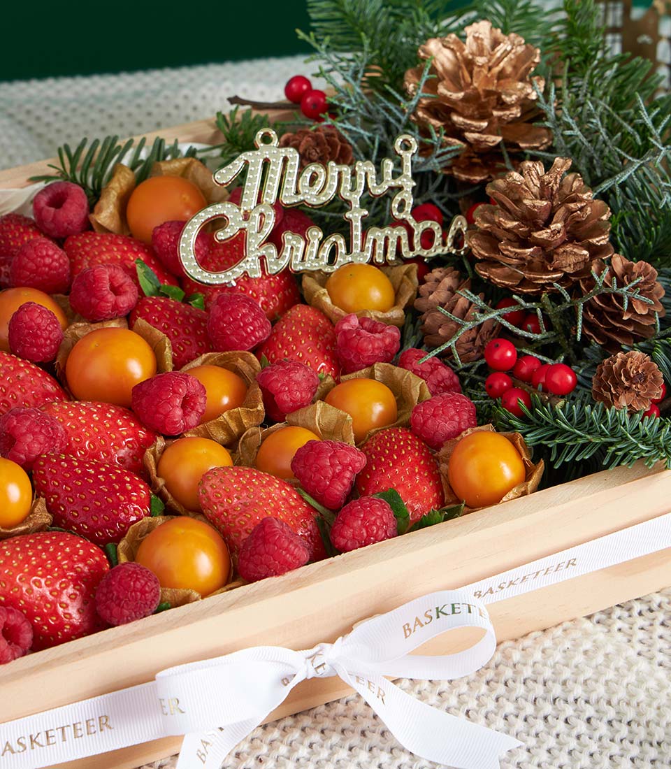 Festive wooden gift box with fresh strawberries, raspberries, and physalis decorated with pine branches and gold accents