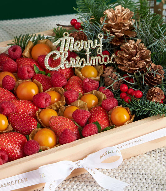 Festive wooden gift box with fresh strawberries, raspberries, and physalis decorated with pine branches and gold accents