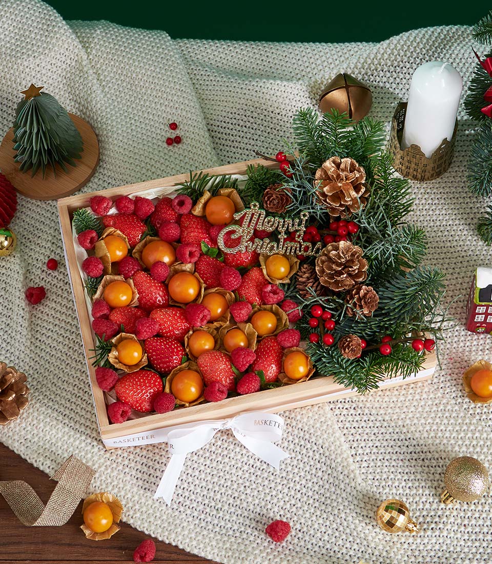 Festive wooden fruit gift box with fresh strawberries, raspberries, and physalis, decorated with Christmas greenery and gold