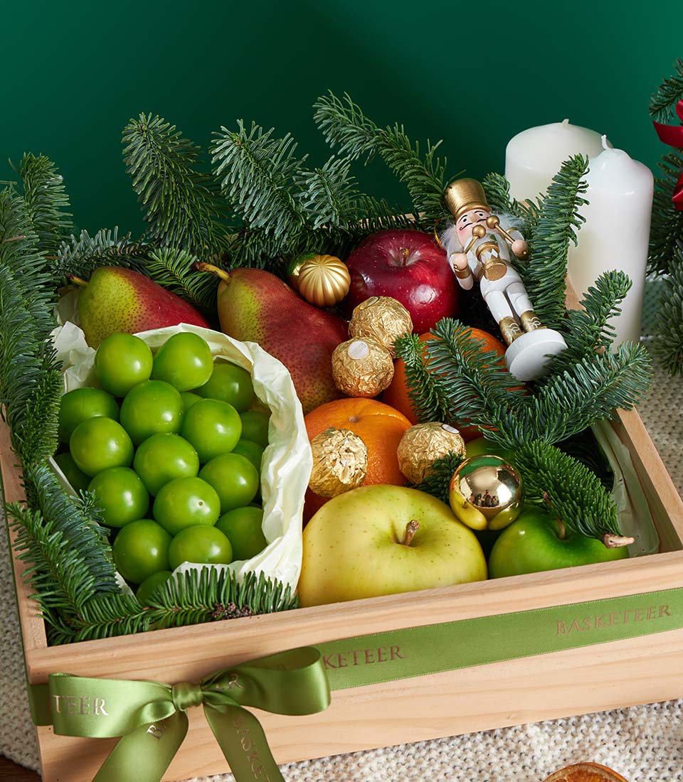 Festive wooden gift box with red pears, apples, plums, Ferrero Rocher chocolates, and holiday ornaments