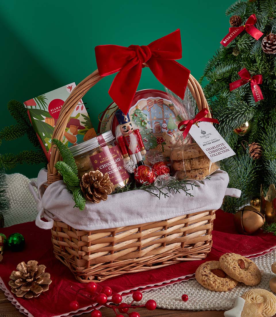 Festive Christmas gift basket with chocolate chip cookies, artisan chocolates, and baked goods in wicker with red velvet bow