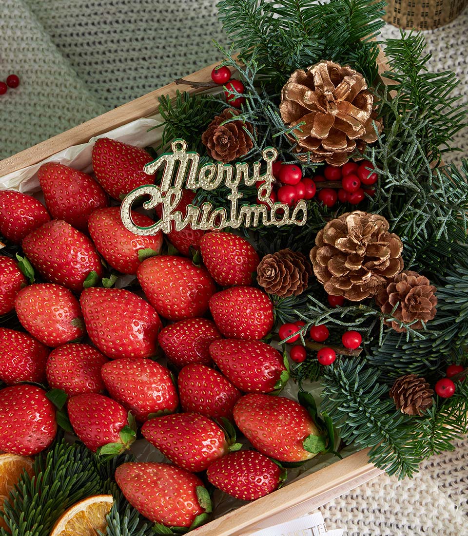 Premium fresh strawberries with festive pine, pinecones, and gold Christmas ornament in luxury wooden gift box