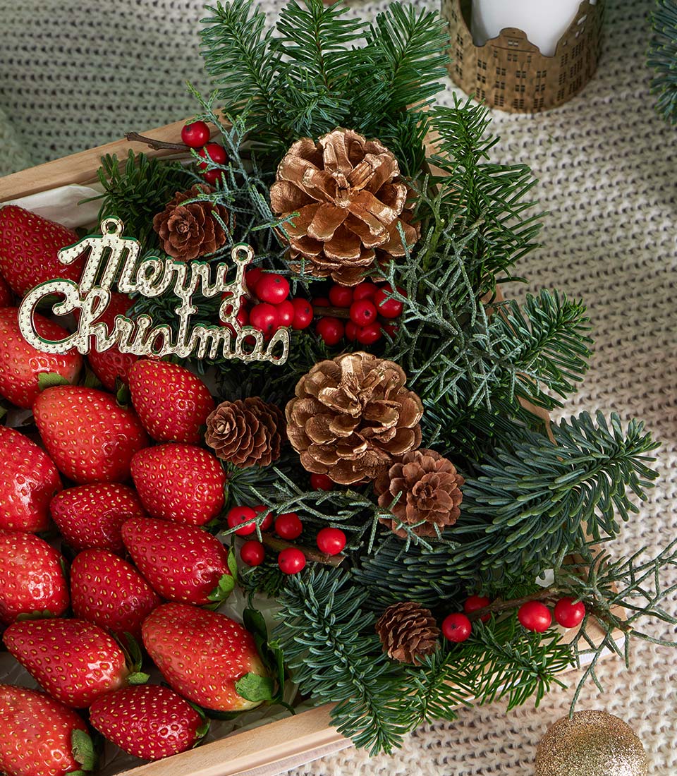 Premium red strawberries with festive pine, pinecones, and berries in wooden Christmas gift box