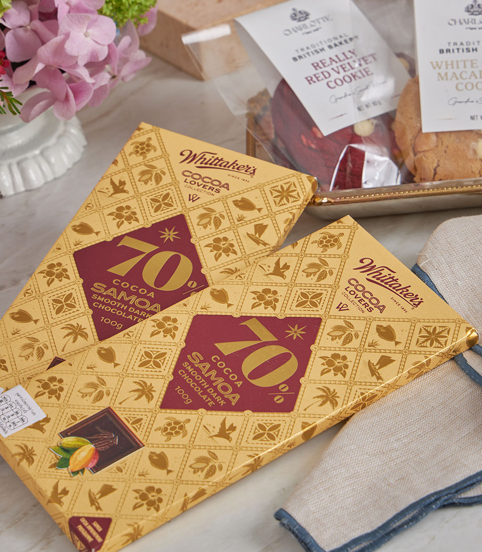 Luxury dark chocolate and British cookies gift basket with gold packaging, fresh pink hydrangeas, and elegant tableware for
