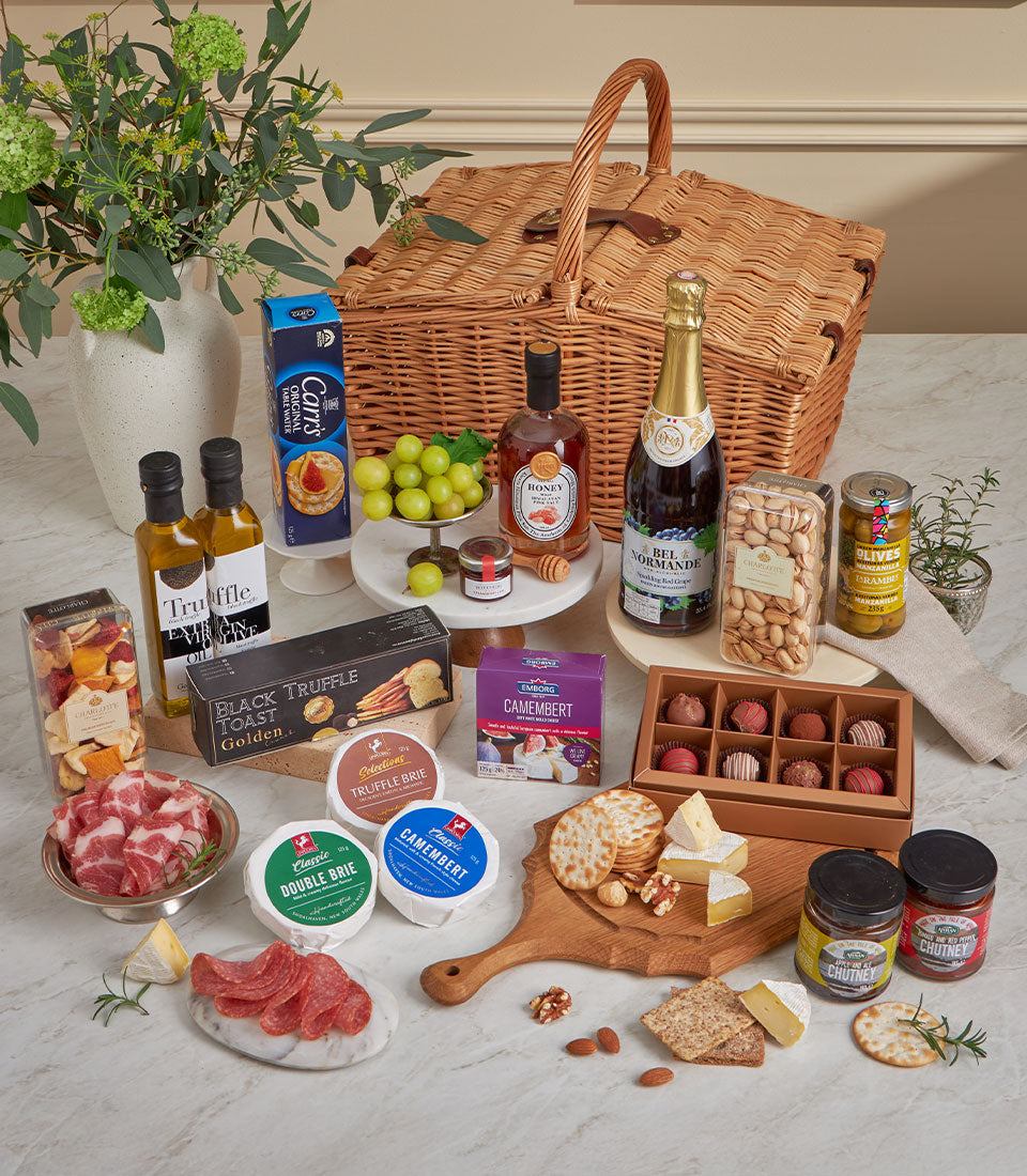 Luxury gourmet picnic basket with artisan cheeses, truffle oil, chocolates, and charcuterie on marble