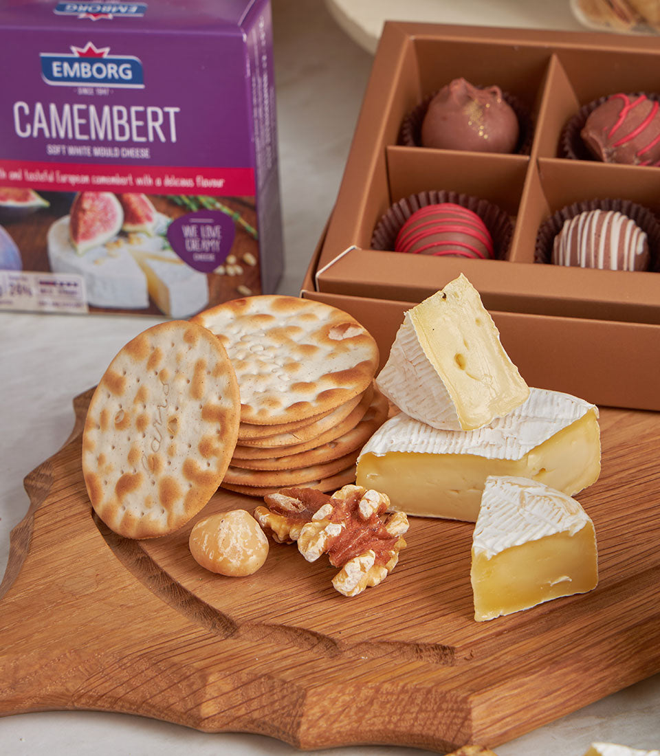 Prestige gourmet gift set with Camembert cheese, artisan crackers, chocolate truffles, and mixed nuts on wooden board