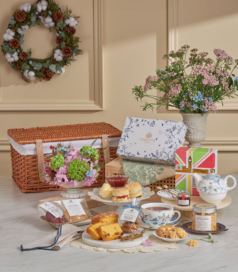 Luxury afternoon tea gift set with scones, Charlotte bakery pastries, Twinings tea, and fresh flowers in wicker basket