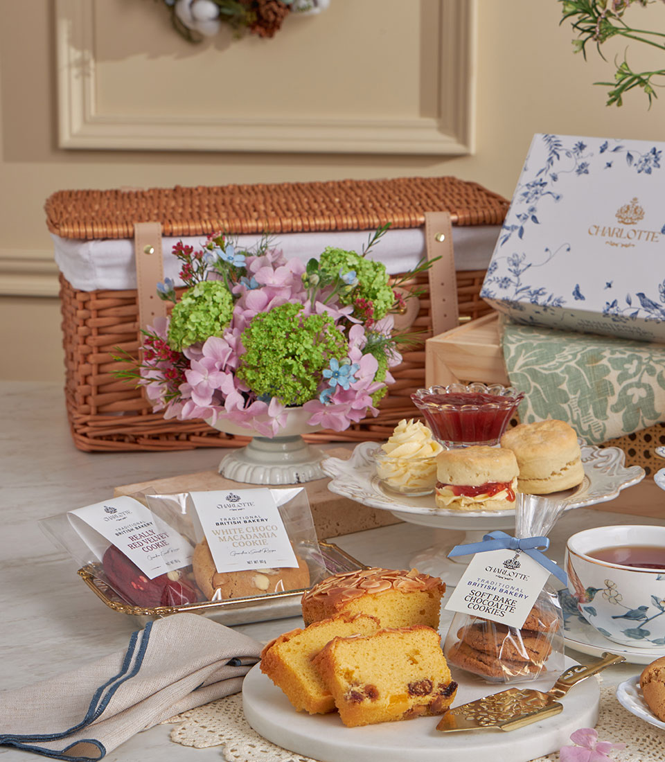 Luxury wicker picnic basket with afternoon tea set, fresh pink hydrangea flowers, tiered scones with clotted cream, gourmet