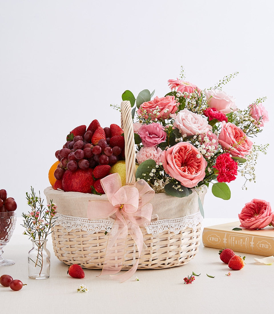 Pink and coral rose arrangement with fresh strawberries, grapes, and apple in white wicker basket, birthday gift