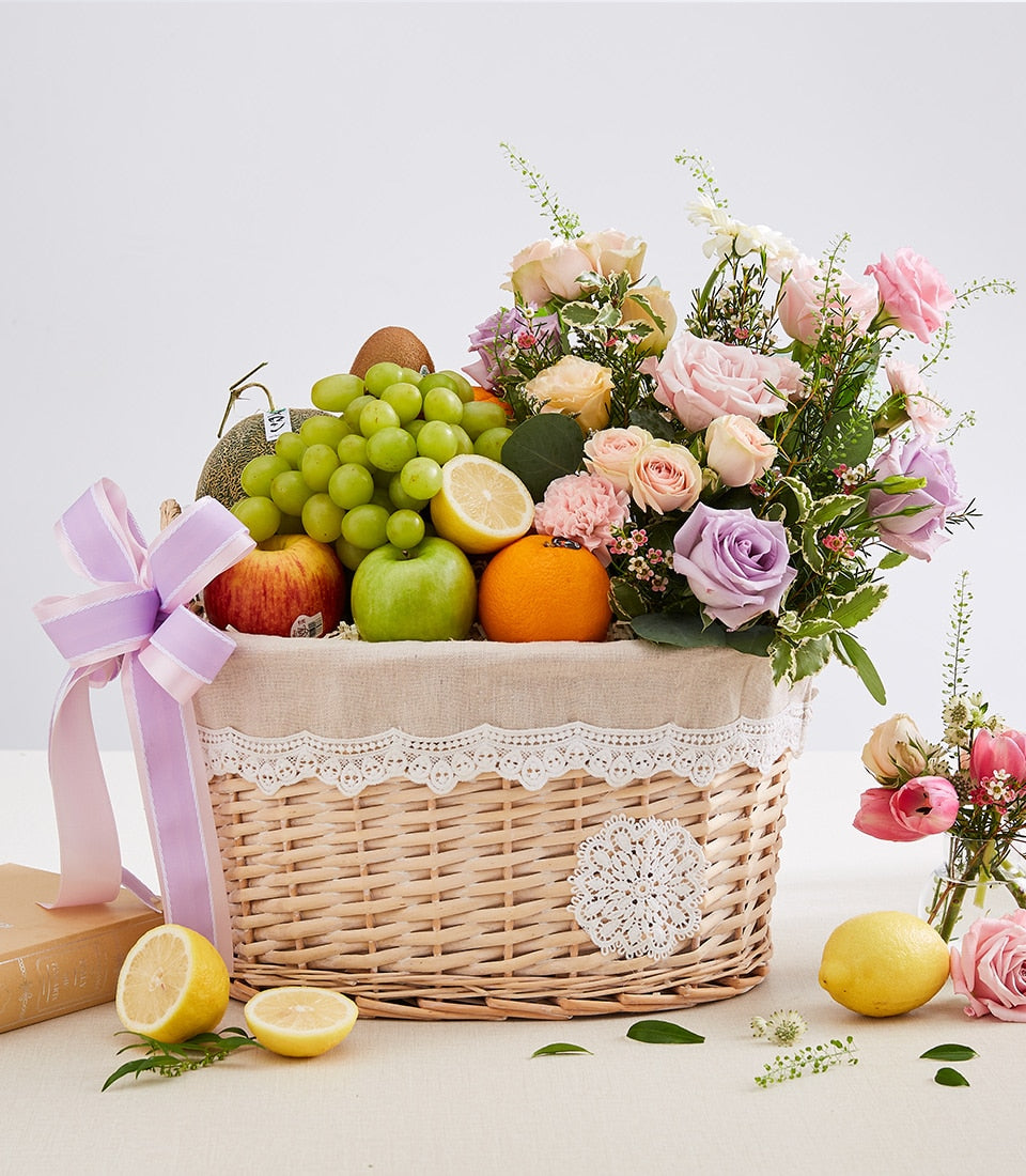 Wicker fruit and flower gift basket with fresh apples, grapes, citrus, lavender and pink roses, white lace trim and purple