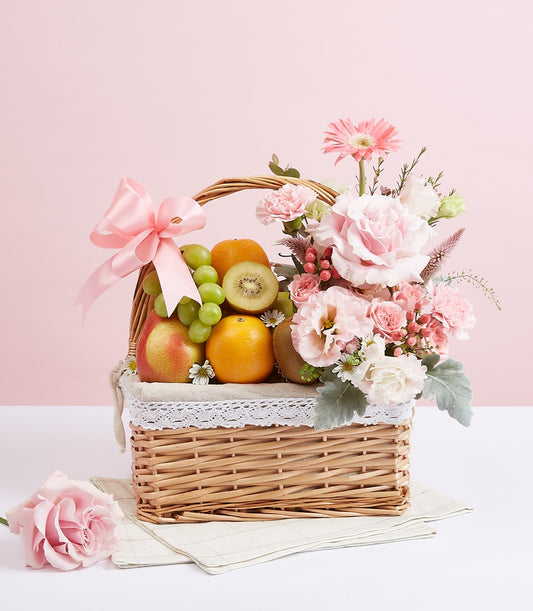 Wicker fruit basket with fresh oranges, kiwis, grapes, pear, and pink rose bouquet tied with ribbon