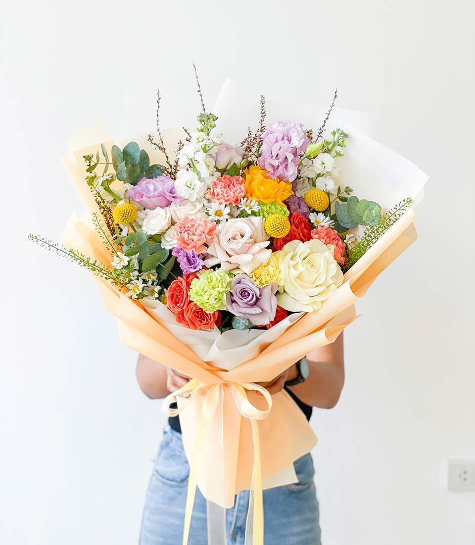 Vibrant mixed flower bouquet with roses, carnations, hydrangeas and snapdragons in peach wrapping