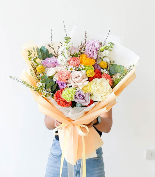 Vibrant mixed flower bouquet with roses, carnations, hydrangeas and snapdragons in peach wrapping