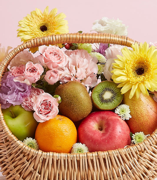 Wicker fruit basket with fresh apples, oranges, kiwi, pear, yellow gerberas, and pink roses for birthdays