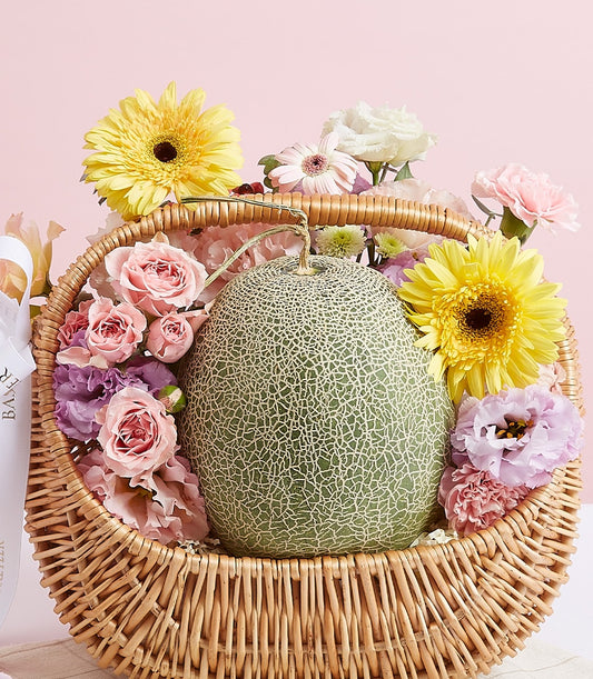 Premium fresh cantaloupe with yellow gerberas, pink roses, and eustoma in wicker gift basket