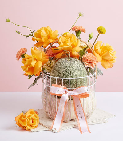Premium cantaloupe melon with yellow roses and peach carnations in luxury gift basket