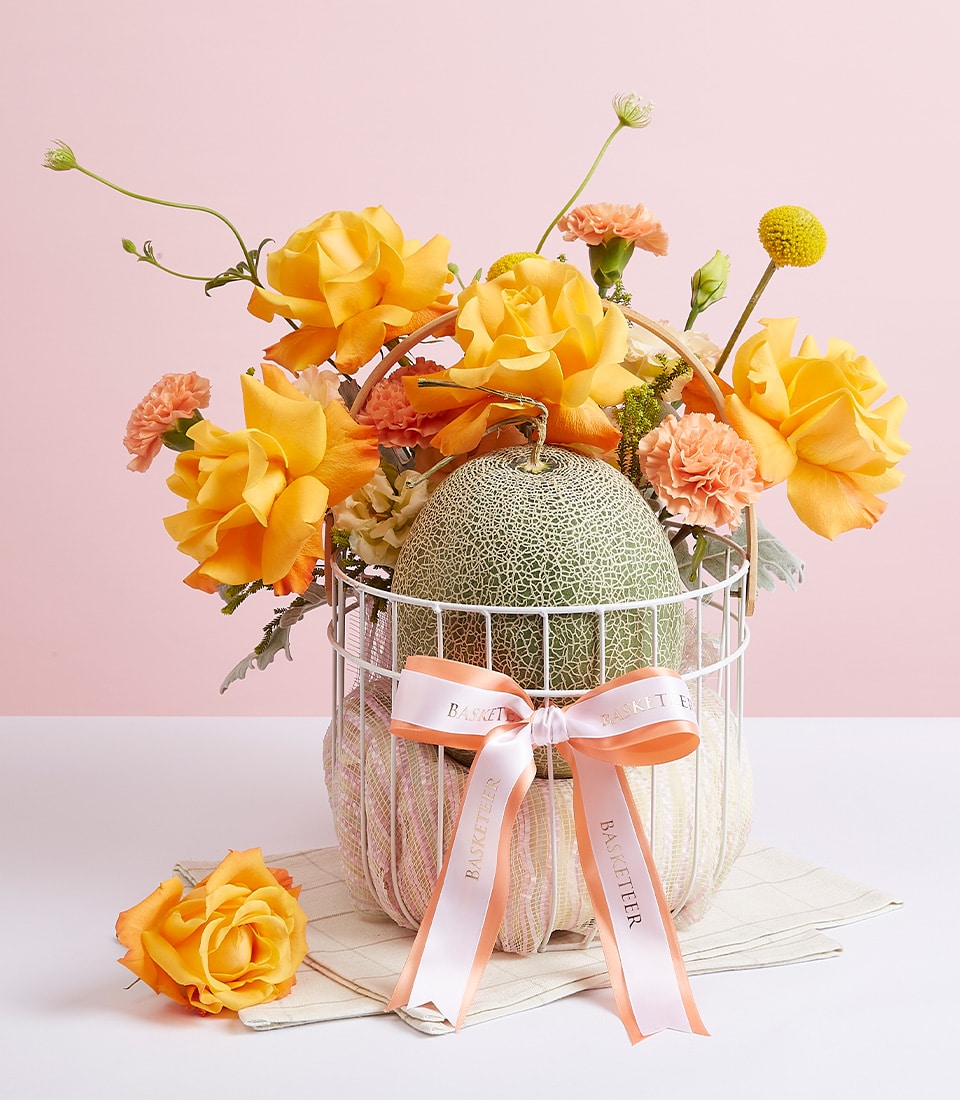 Premium cantaloupe melon with yellow roses and peach carnations in luxury gift basket