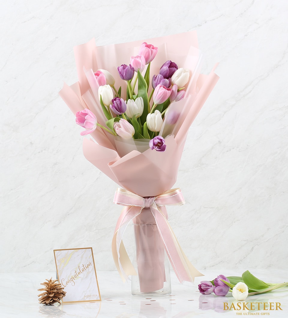 Fresh pink, purple, and white tulips arranged in glass vase with ribbon, perfect for birthday celebrations