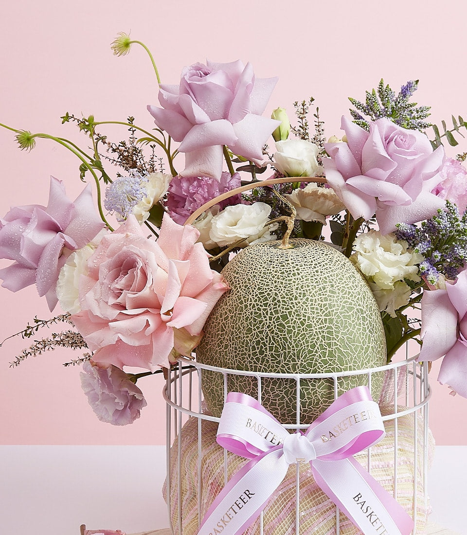 Fresh cantaloupe with premium roses and mixed flowers in white wire gift basket