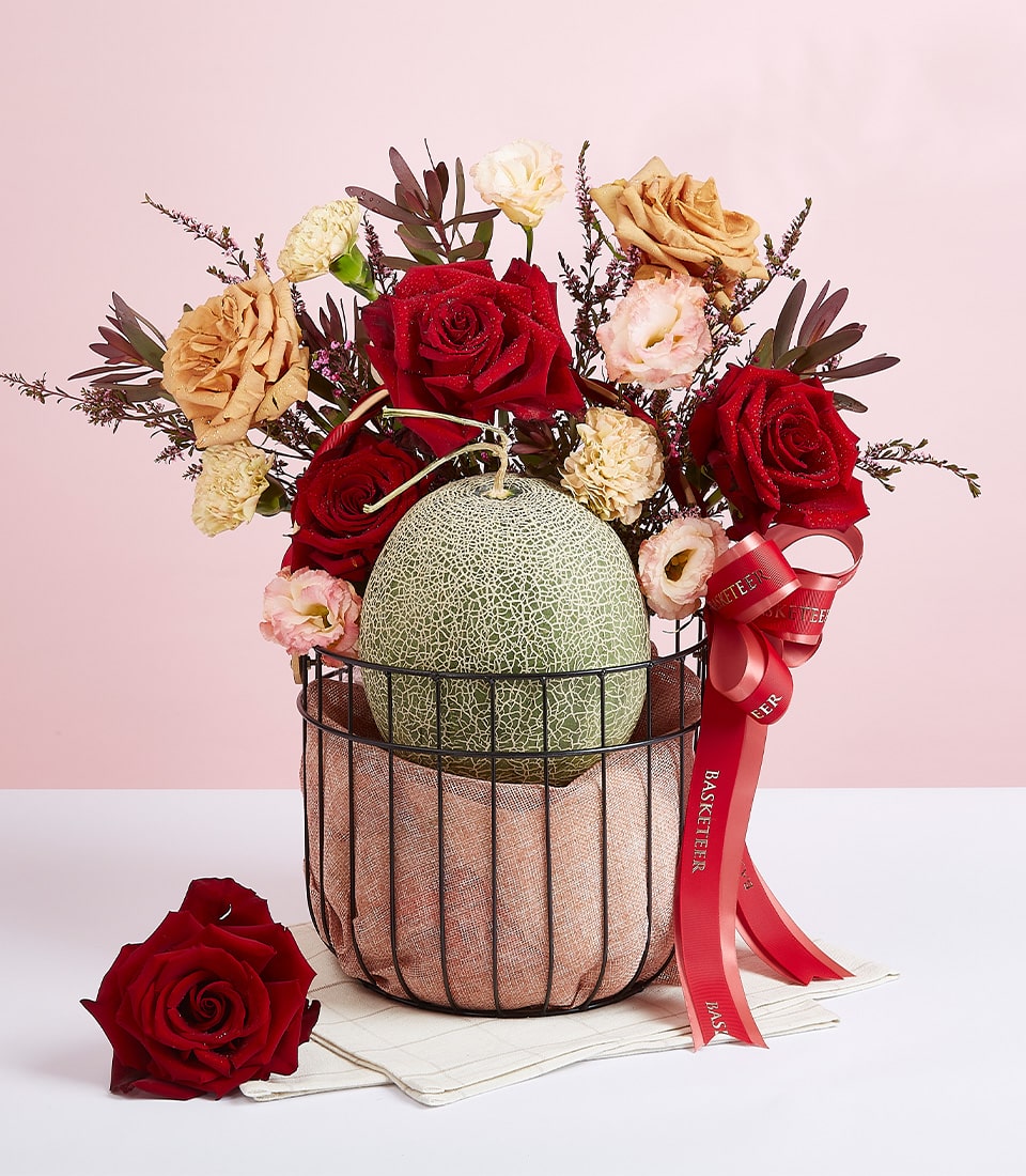 Fresh cantaloupe melon with deep red and peach roses in black wire basket lined with pink fabric