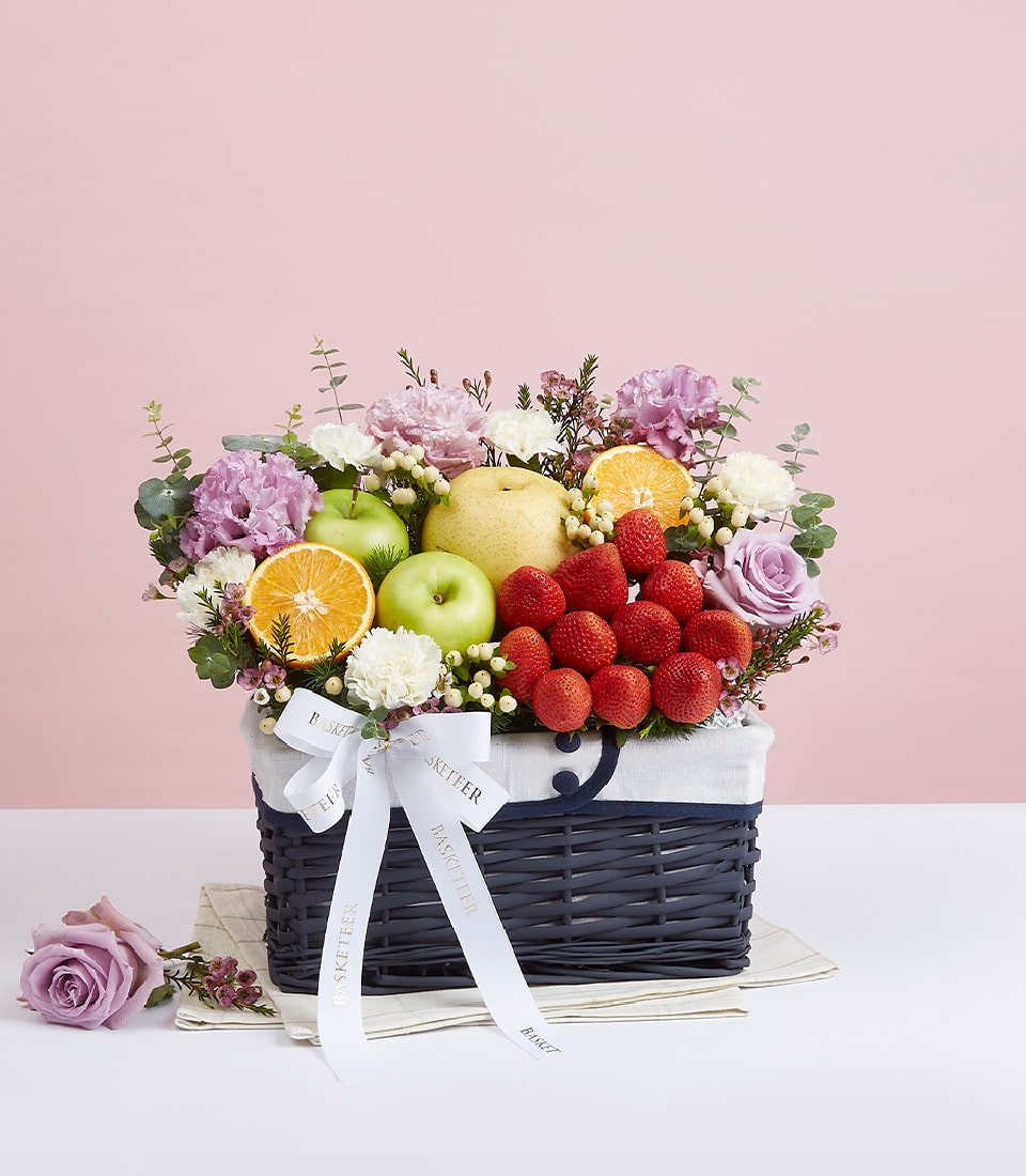 Deluxe purple roses and fresh fruit gift basket with strawberries, apples, and carnations on woven base