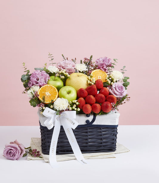 Deluxe purple roses and fresh fruit gift basket with strawberries, apples, and carnations on woven base