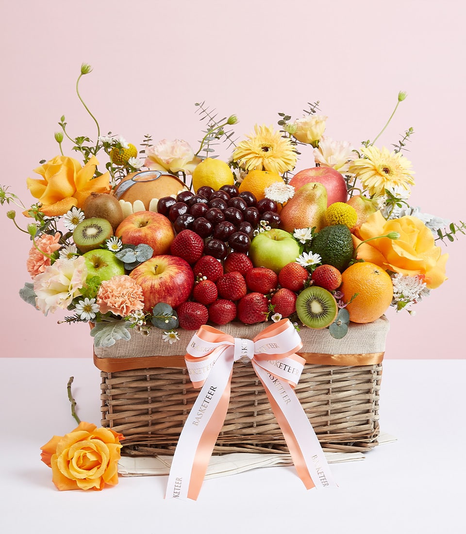 Woven wicker fruit basket with fresh apples, kiwis, strawberries, oranges, and yellow roses for birthdays